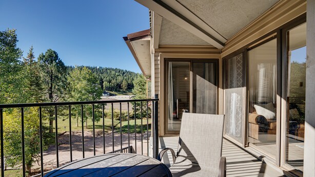 Un balcon avec une table et des chaises, une vue sur une forêt et un bâtiment doté de grandes portes vitrées.