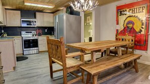 Cozinha com armários de madeira, eletrodomésticos de aço inoxidável e mesa de jantar de madeira com bancos.
