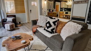A cozy living room with a grey sofa, a wooden coffee table, and a brown leather armchair.