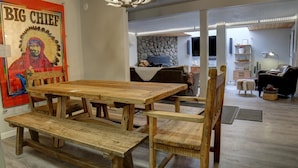 A dining area with a wooden table and benches, a stone wall in the background, and a poster on the wall.