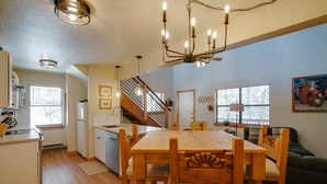 A spacious kitchen with wooden cabinets, a dining table with chairs, a staircase, and a living area with a sofa.