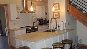 A modern kitchen with a central island, bar stools, stainless steel appliances, and pendant lighting.