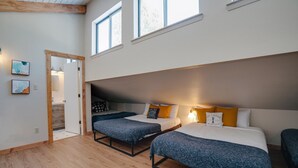 A modern hotel room with two beds, wooden flooring, large windows, and artwork on the walls.