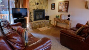 Ein Wohnzimmer mit Kamin aus Stein, Ledersofas, einem Fernseher und einem kleinen Tisch mit Dekoration.
