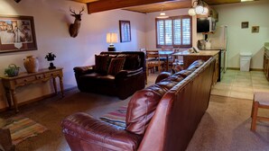 Ein gemütliches Wohnzimmer mit einer Ledersofa, einem Essbereich mit Tisch und Stühlen, einem aufgehängten Hirschgeweih und einer Küchenzeile mit Kühlschrank und Spüle.