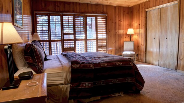 Ein Zimmer in einer Holzhütte mit einem Bett, einem Sessel, einem Schreibtisch und einer Lampe.