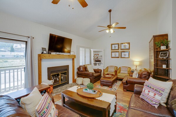 A cozy living room with leather sofas, a wooden coffee table, a fireplace, and a ceiling fan. - Townhome close to the base area (Angel Fire)
