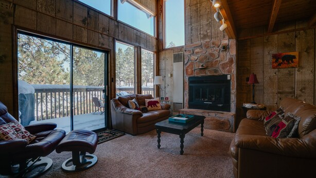 Un salón acogedor con chimenea de piedra, sofás de cuero y amplias ventanas con vistas a una terraza nevada.