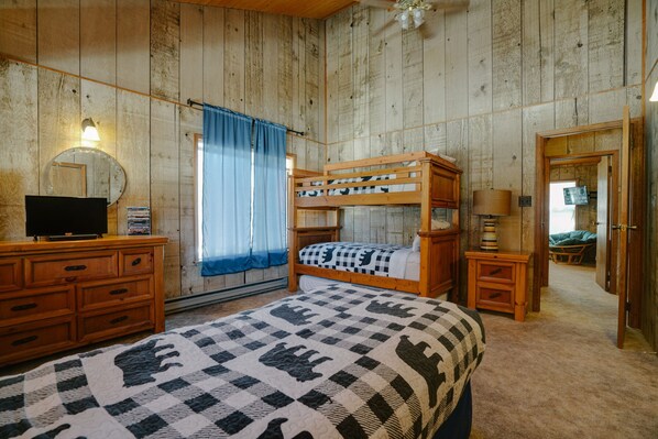 A bedroom with a bunk bed, a desk with a television, a mirror, and a window with curtains.