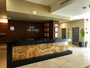 Un mostrador de recepción de hotel con encimera de mármol, un reloj y un cartel de recepción.