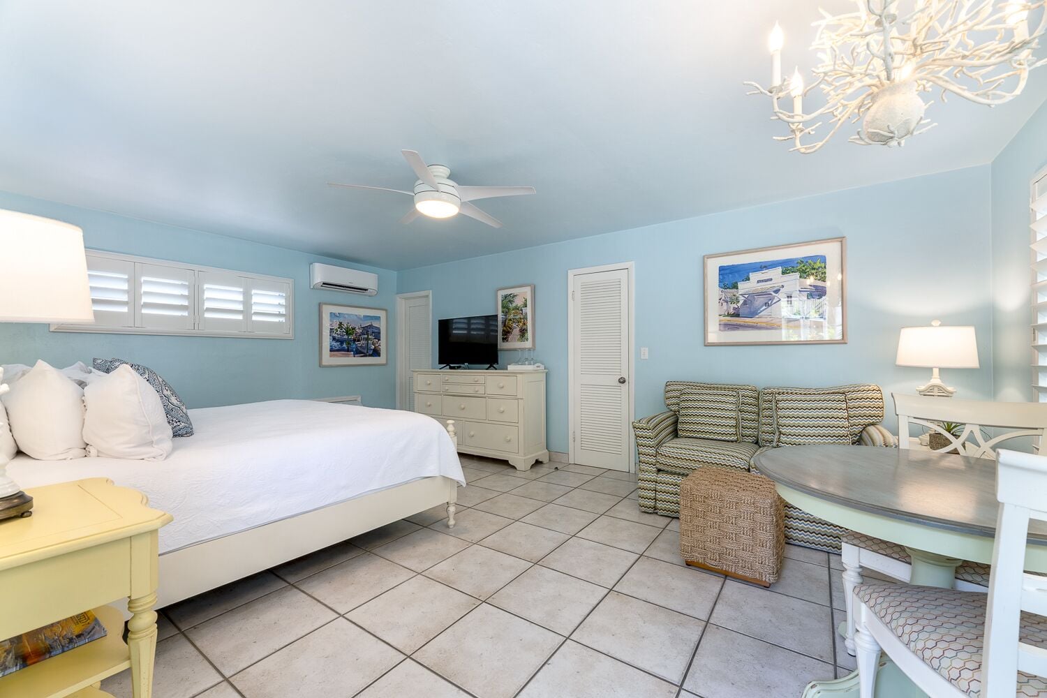 A bedroom with a bed, bedside table, dresser, TV, and a seating area with a table and chairs.
