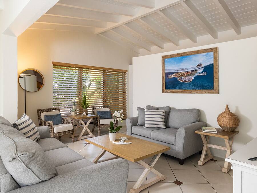 Een moderne woonkamer met een grijze bank, een houten salontafel, rieten stoelen en een groot schilderij van een zeeschildpad.