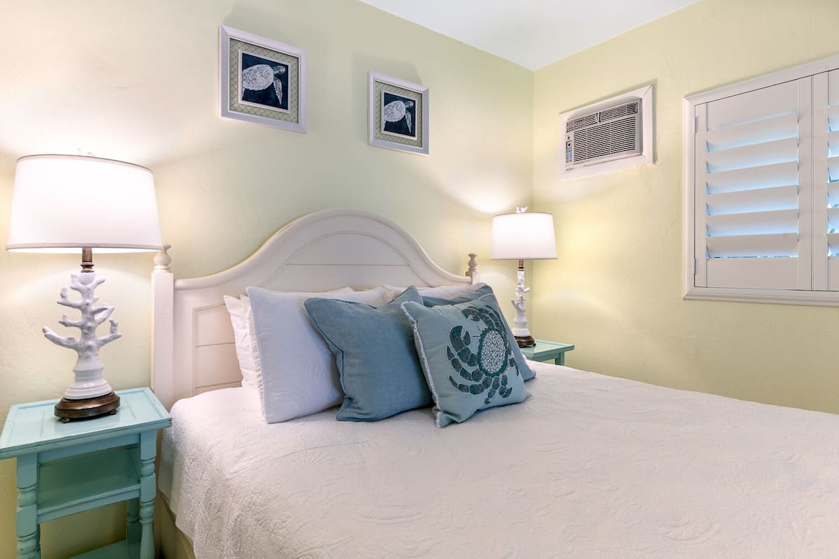Une chambre à coucher avec un lit, deux tables de chevet, deux lampes et deux tableaux encadrés accrochés au mur.