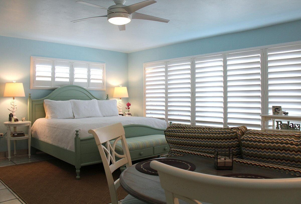 A bedroom with a bed, two bedside tables, a chair, a sofa, and a ceiling fan.