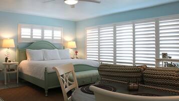 A bedroom with a bed, two bedside tables, a chair, a sofa, and a ceiling fan.