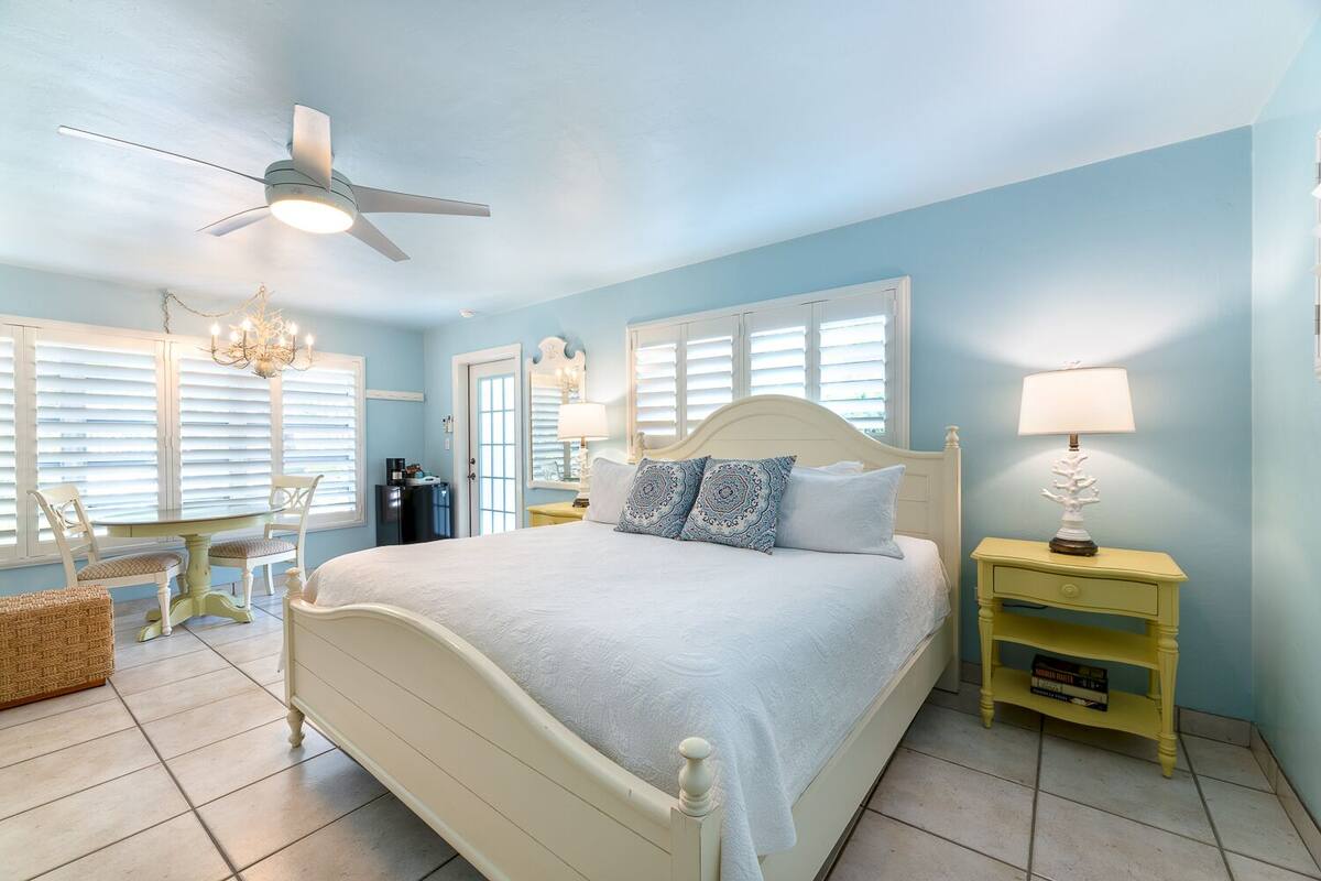 Une chambre à coucher comprenant un lit, une table de chevet, une chaise, une table et un ventilateur de plafond.