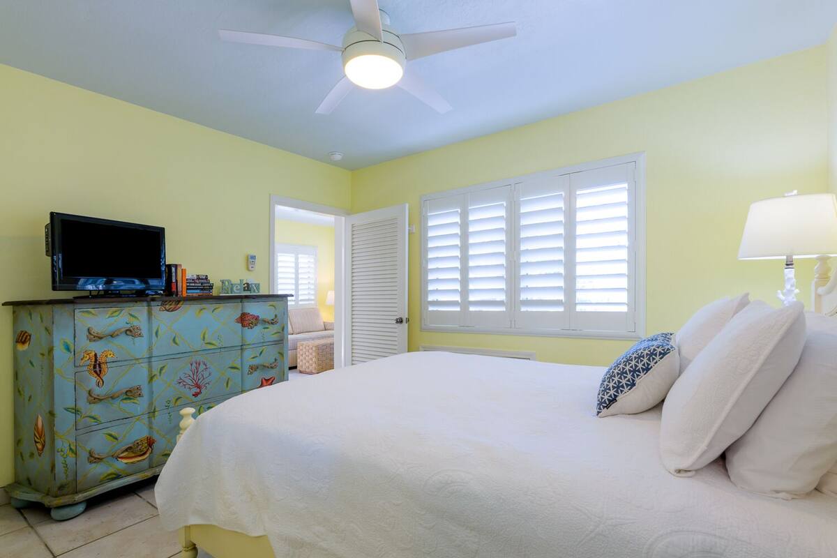 Une chambre à coucher avec un lit, un téléviseur posé sur une commode et un ventilateur de plafond.