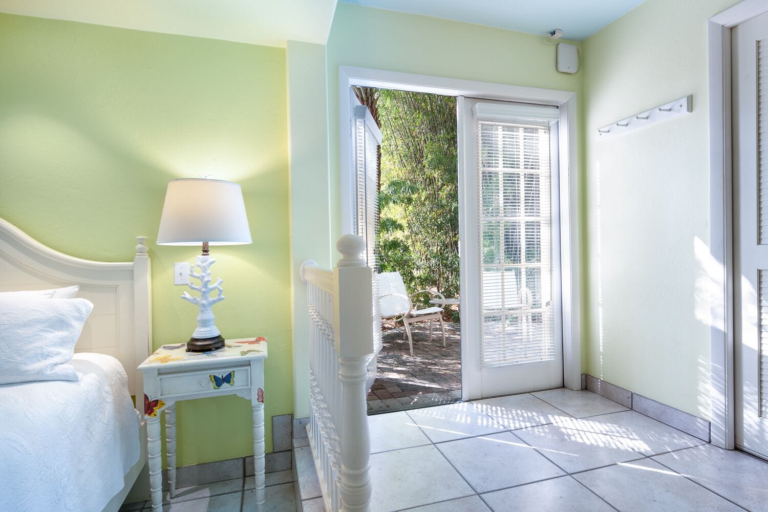 Una habitación con una cama, una mesita de noche con lámpara, una ventana con persianas y vista a la vegetación.