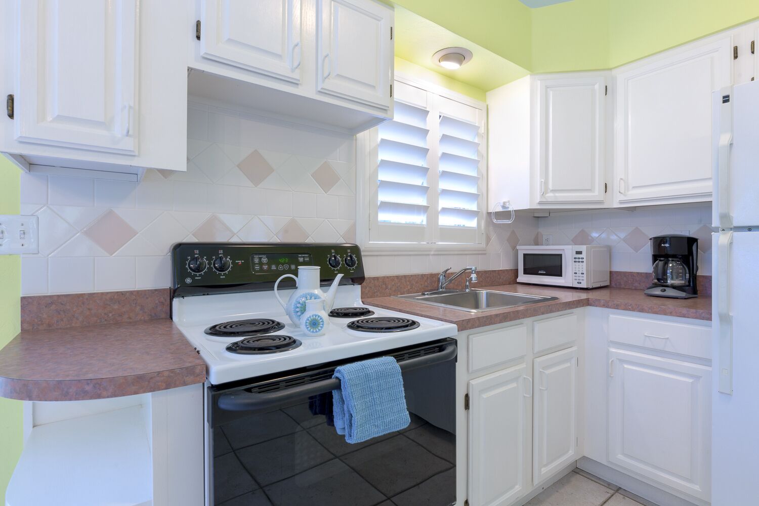 A kitchen with white cabinets, a stove, a sink, and a microwave.