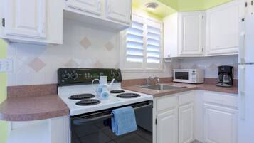A kitchen with white cabinets, a stove, a sink, and a microwave.