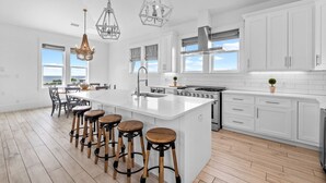 Une cuisine moderne avec des meubles blancs, un grand îlot central doté de tabourets, des appareils en acier inoxydable et un éclairage suspendu.