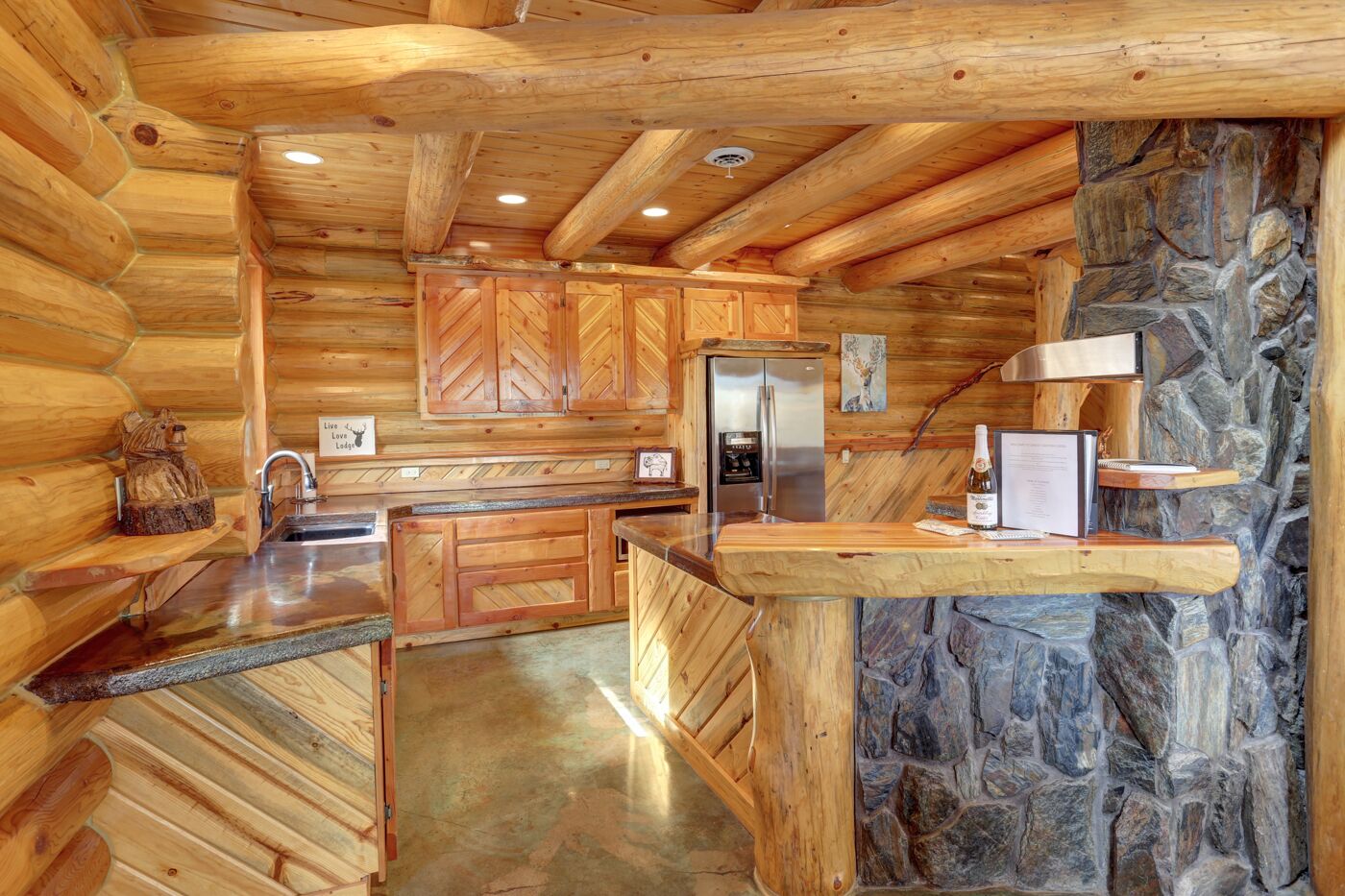 Une cuisine de style rustique, avec des meubles en bois, un mur d’accent en pierre et un réfrigérateur encastré.
