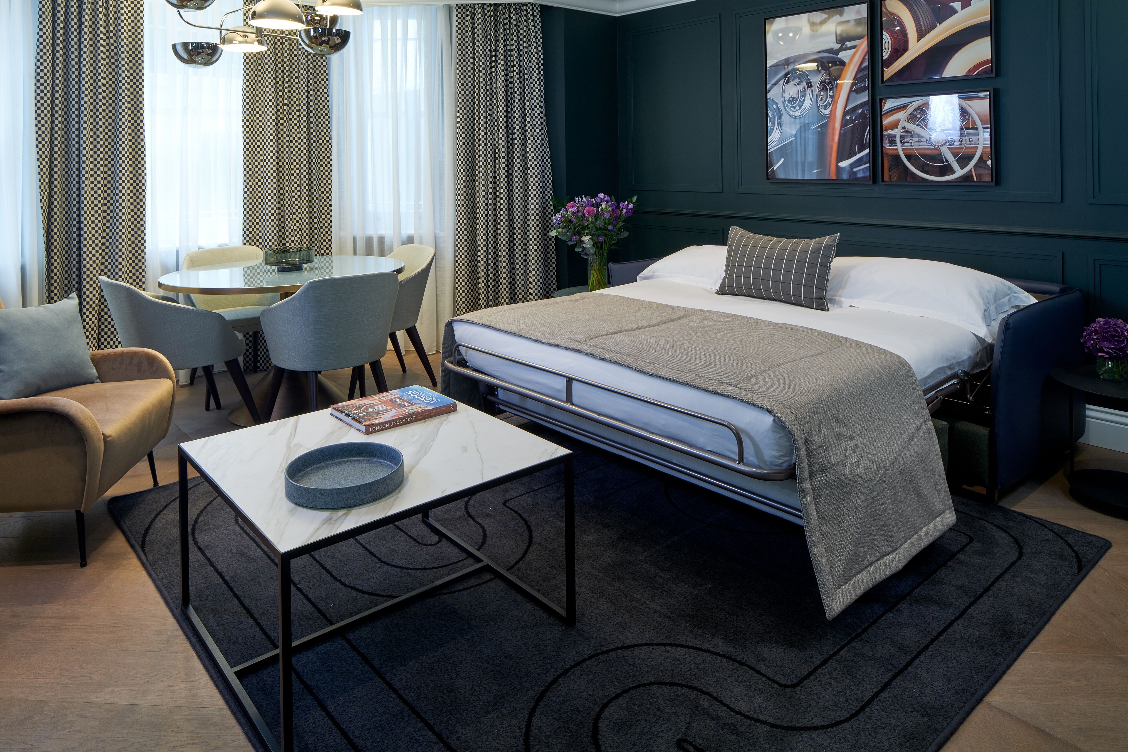 A modern hotel room with a bed, a dining table, chairs, a sofa, and a coffee table.