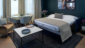 A modern hotel room with a bed, a dining table, chairs, a sofa, and a coffee table.