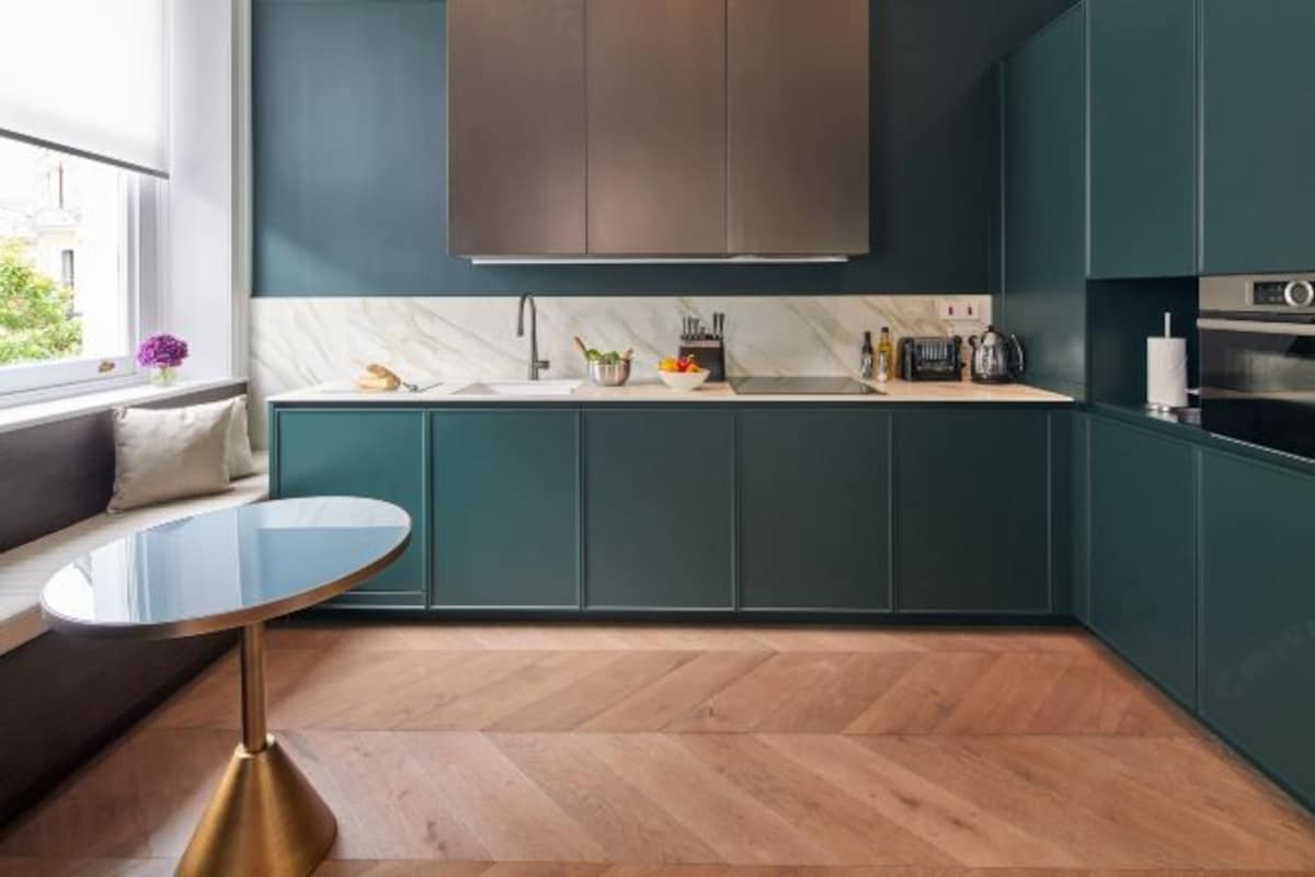 Una cocina moderna con armarios verde azulado, encimera de mármol y suelo de madera con diseño de espiga.