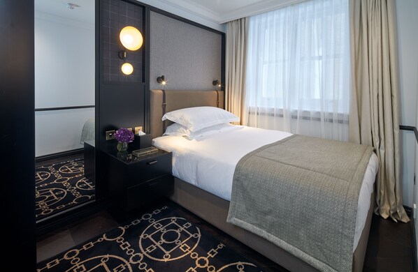 A hotel room with a bed, bedside table, lamp, and a large window with curtains. - Lexham Gardens by Cheval Maison (London)
