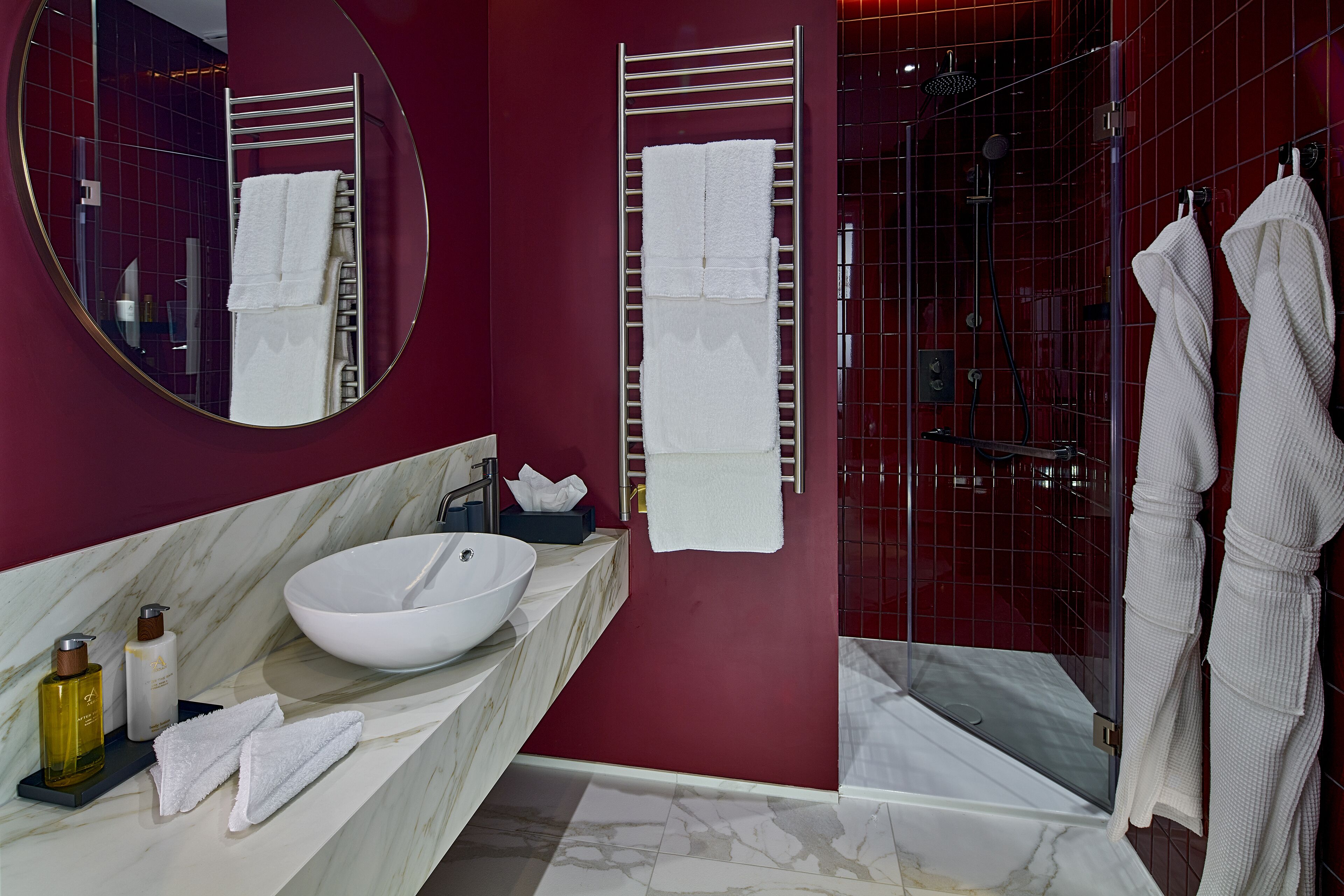 A modern bathroom with a large round mirror, a white sink, and a glass-enclosed shower.