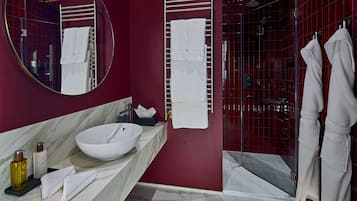 A modern bathroom with a large round mirror, a white sink, and a glass-enclosed shower.