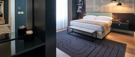 A modern bedroom with a large bed, a bedside table with a lamp, and a view of the hallway.
