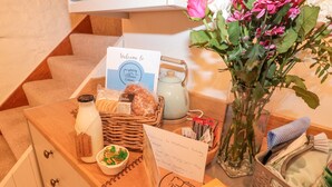 A reception desk with a welcome card, a basket of bread, a milk bottle, a vase of flowers, and a guest book. - Honeysuckle Cottage (Paignton)