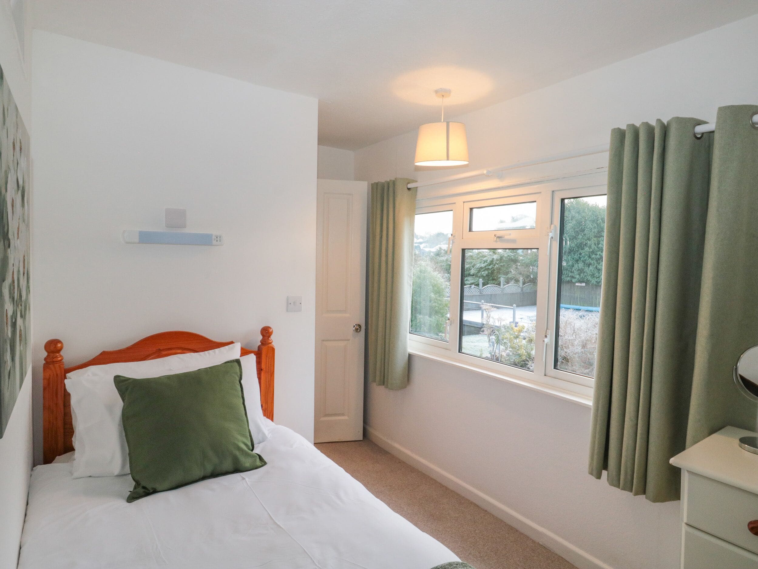 A bedroom with a wooden bed, a window with curtains, a bedside table, and a hanging light fixture.
