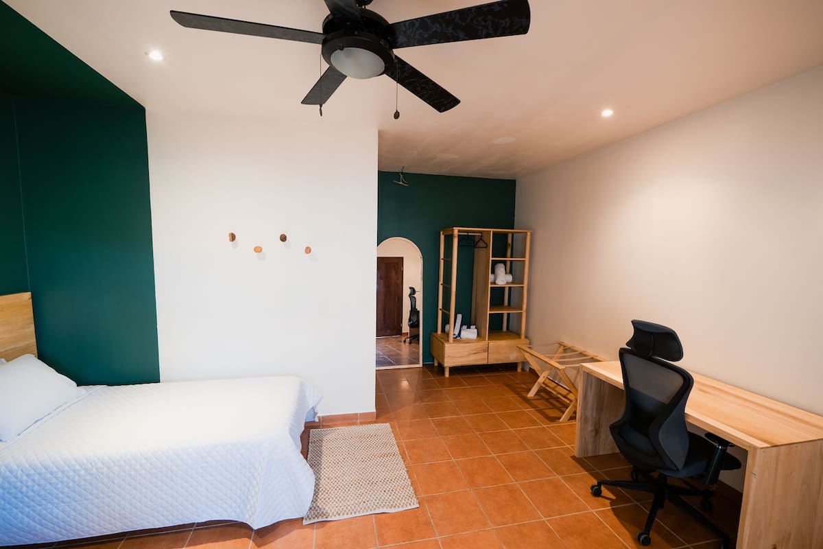 A bedroom with a bed, a desk, a chair, a wardrobe, and a ceiling fan.