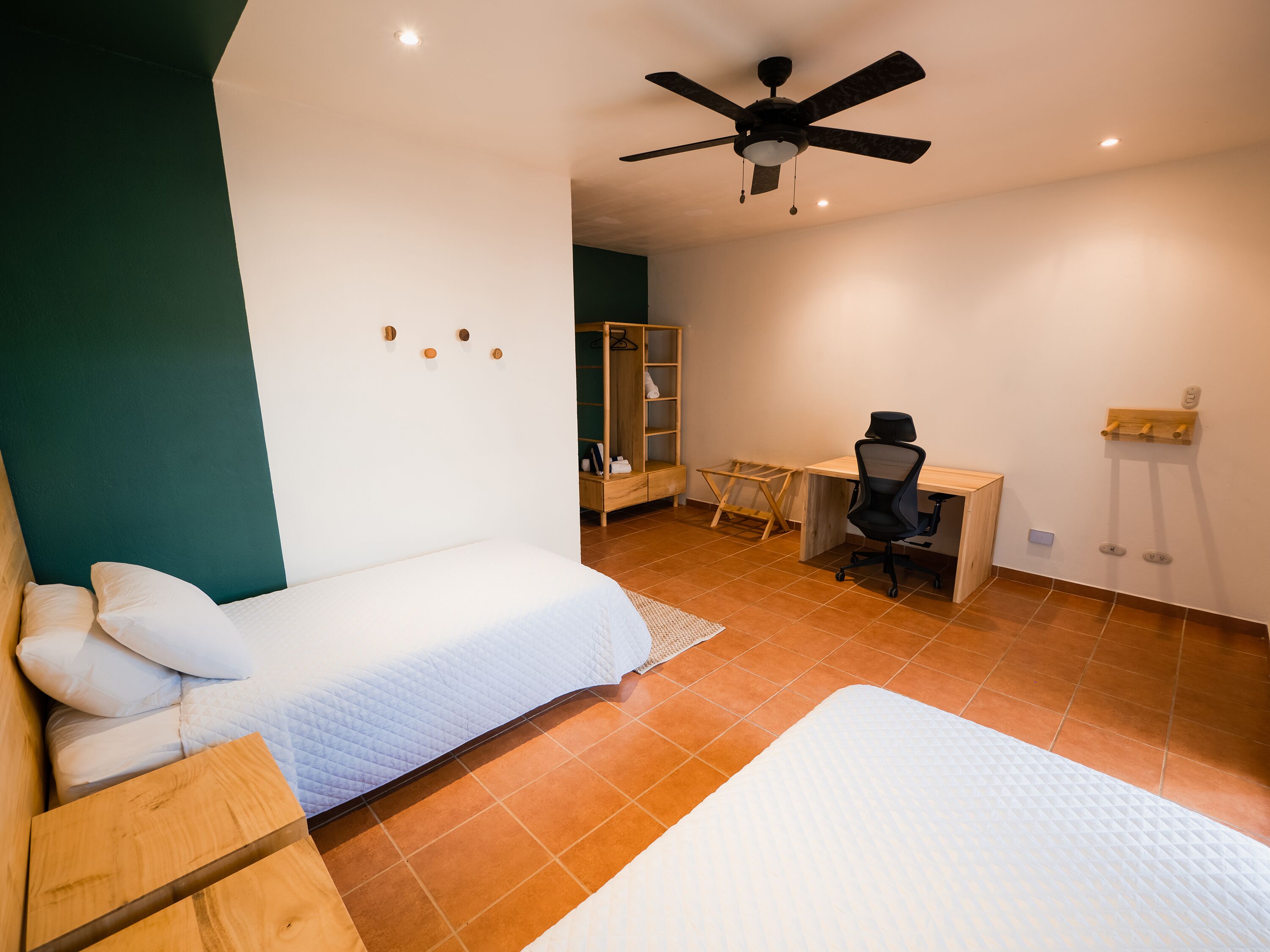 Een slaapkamer met een bed, bureau, stoel, kledingkast en plafondventilator.