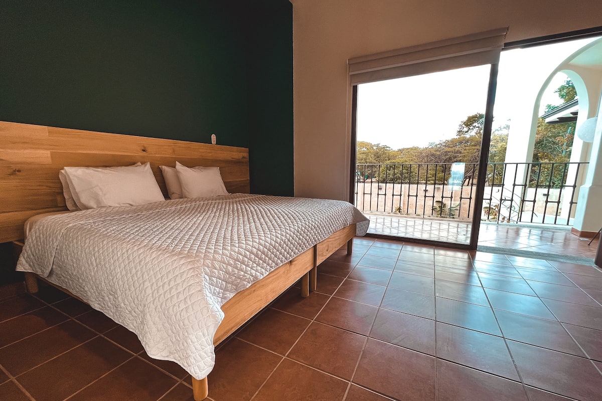 A bedroom with a wooden bed, white bedding, and a view of a balcony with a railing.