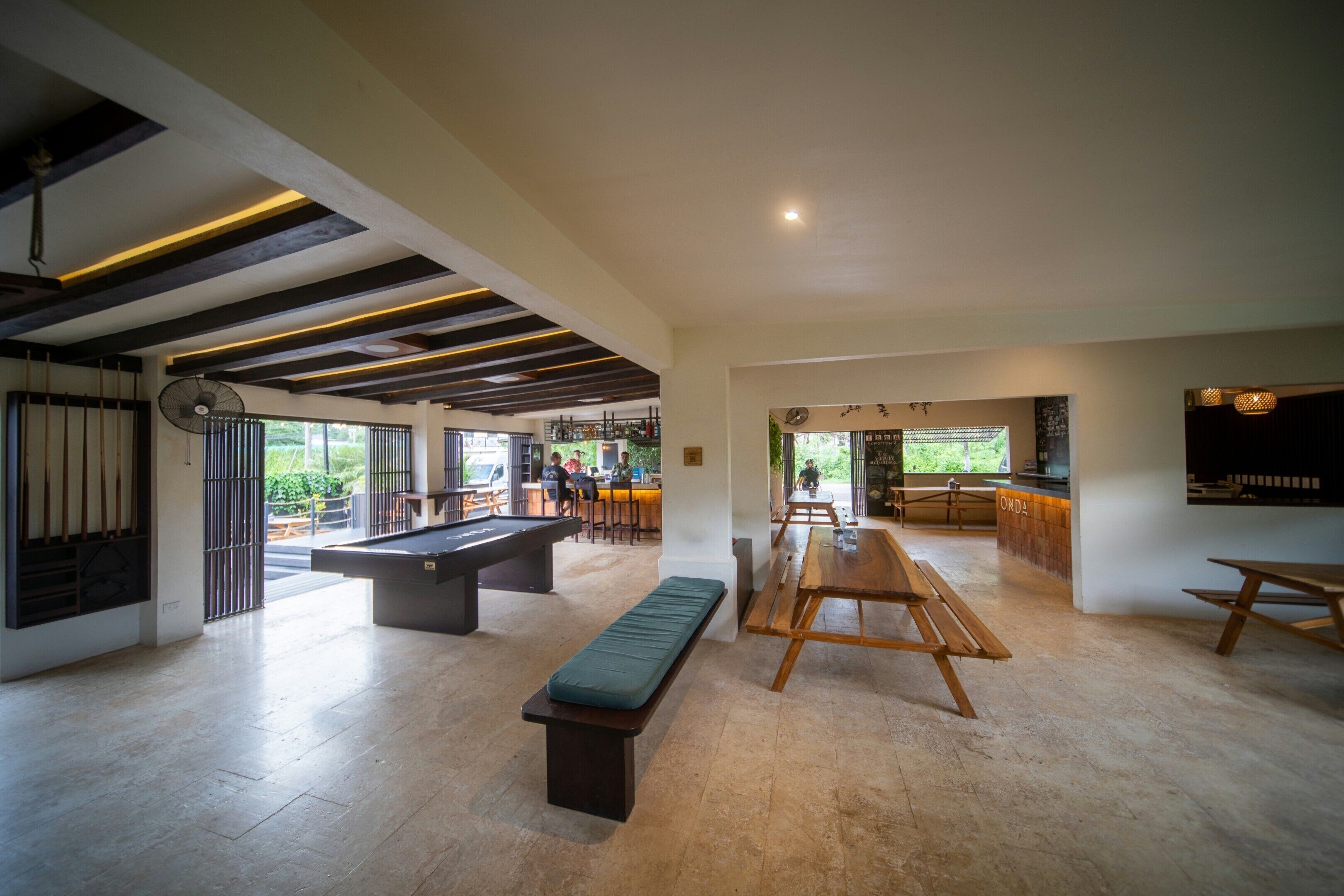A spacious indoor area with a pool table, a bench, and a long table, likely part of a hotel or resort.