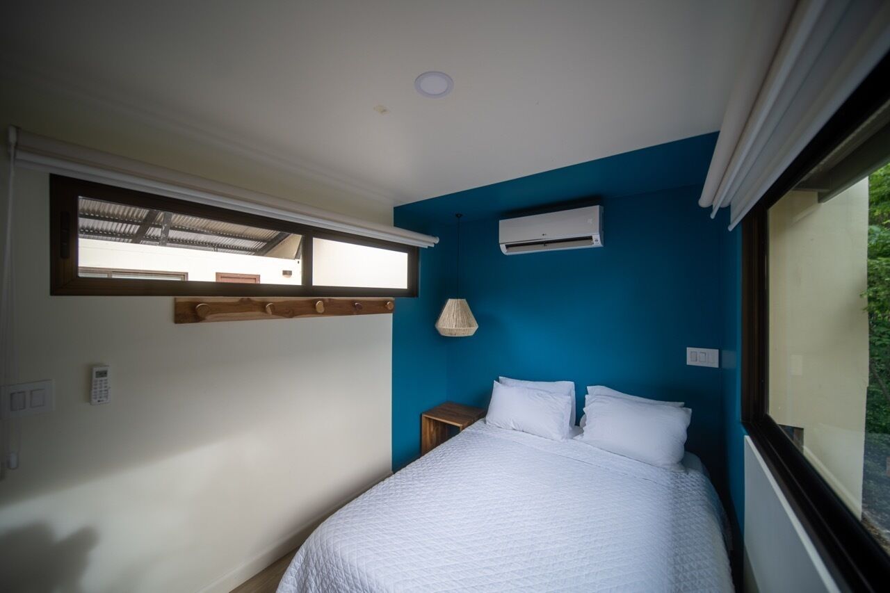 Un dormitorio con cama, ventana, aire acondicionado y una mesita de noche.