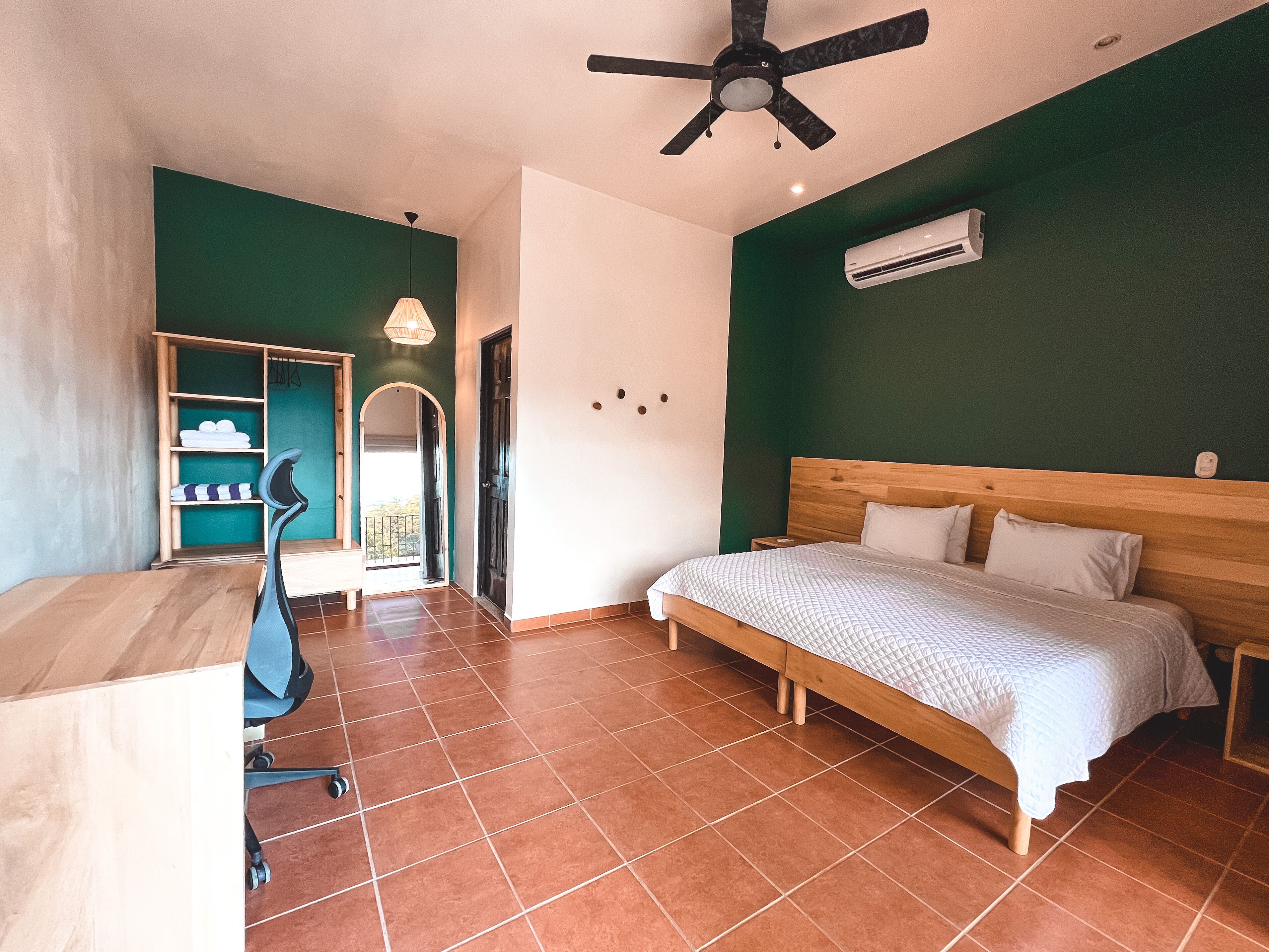 A bedroom with a bed, desk, chair, and an air conditioning unit.