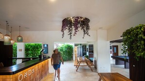 A reception area with a wooden counter labeled "ONDA," a wooden bench, and hanging plants. - ONDA - Playa Grande - Adults Only (Cabo Velas)