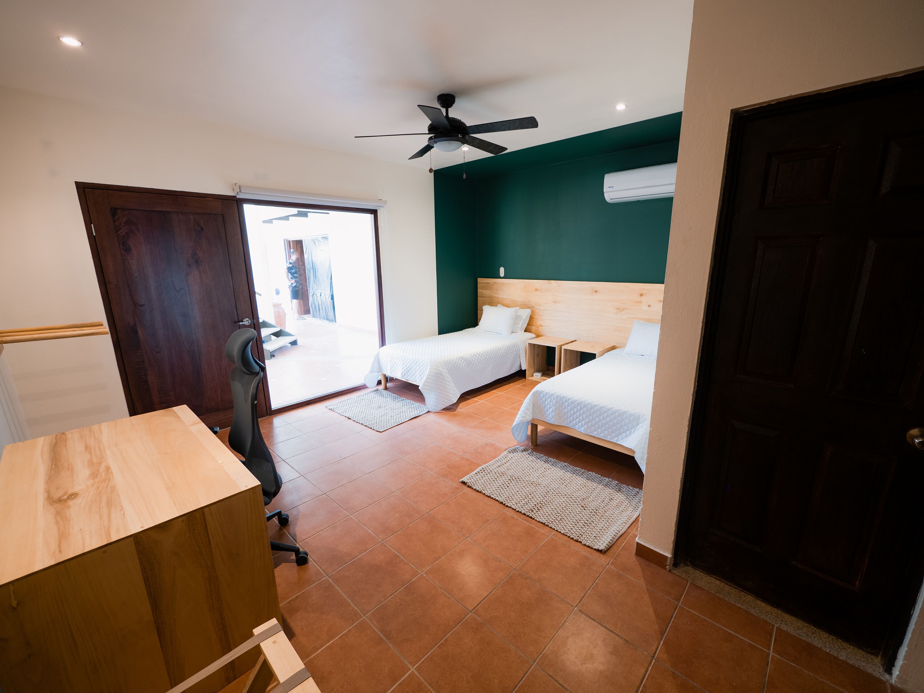 Una habitación con dos camas, ventilador de techo y puerta que da a un espacio exterior.