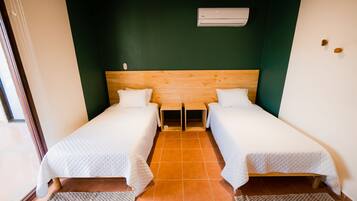 Een kamer met twee eenpersoonsbedden, een houten hoofdbord, een airconditioning en een betegelde vloer.
