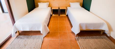A room with two single beds, a wooden headboard, an air conditioning unit, and a tiled floor.