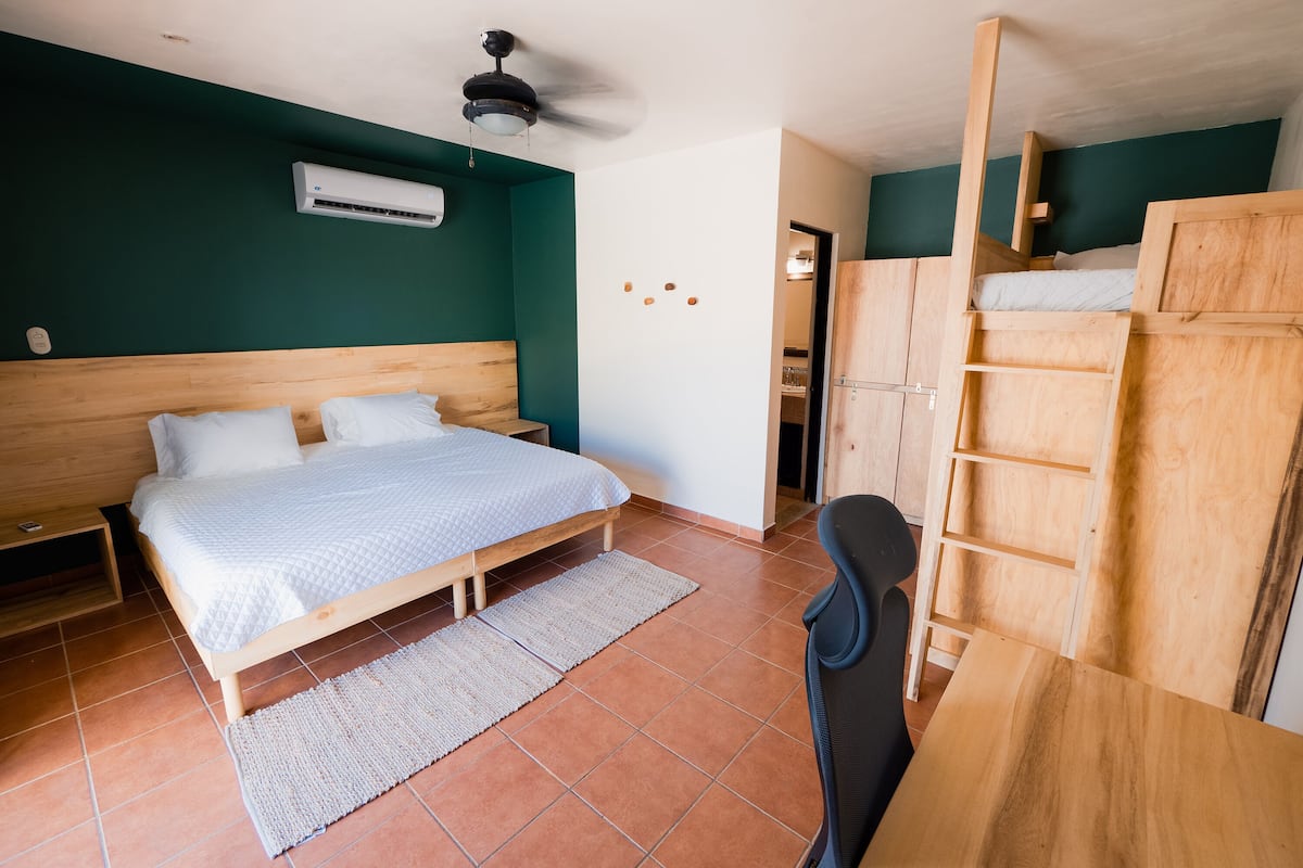 A bedroom with a bed, a desk, a chair, a ceiling fan, and an air conditioning unit.