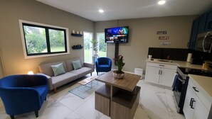 Un salon moderne avec un canapé, deux fauteuils bleus, une table basse et un téléviseur fixé au mur.