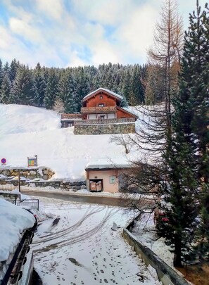 A wooden chalet with a balcony, surrounded by snow-covered trees and a mountain backdrop. - Cosy apartment in Courchevel 1550 (Courchevel)