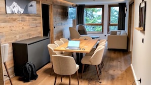 A modern, well-lit room with a wooden wall, a dining table with chairs, a sofa, and a TV mounted on the wall. - Cosy apartment in Courchevel 1550 (Courchevel)