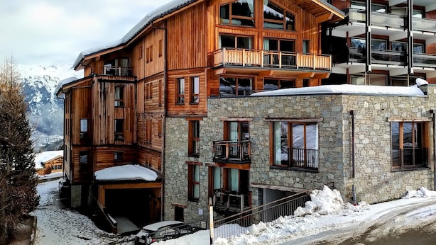 A multi-story wooden building with balconies and a stone extension, surrounded by snow. - Cosy apartment in Courchevel 1550 (Courchevel)